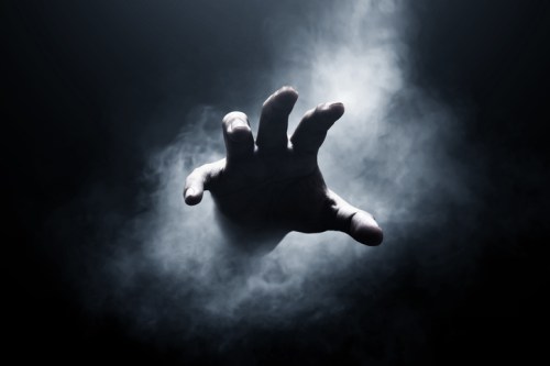 A ghostly hand reaches out from a dark, smoky background, creating a mysterious and eerie atmosphere.