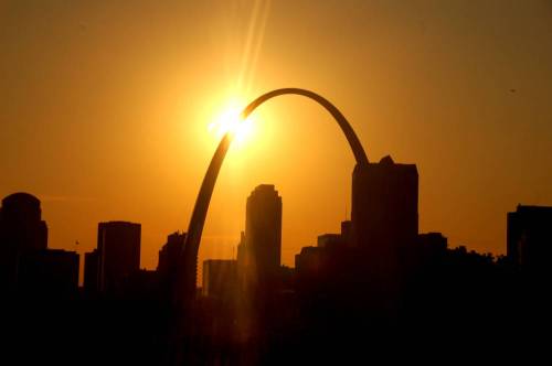 Silhouette of the Gateway Arch against a vibrant sunset, with city skyline in the foreground.