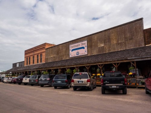 A rustic storefront with a sign reading "Quintero's Store," featuring parked cars and flower planters along the porch.