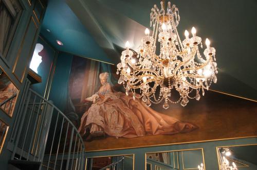 A grand chandelier hangs in a room with teal walls and a large mural of a woman in a gown. A spiral staircase is visible.