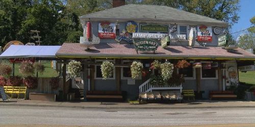 A quaint restaurant with colorful signage and hanging flower baskets, set in a rural area.