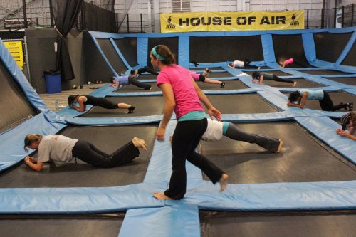 A group of people exercising on trampolines at a trampoline park, with an instructor guiding them.