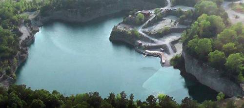 Aerial view of a serene blue lake surrounded by green trees and rocky terrain.