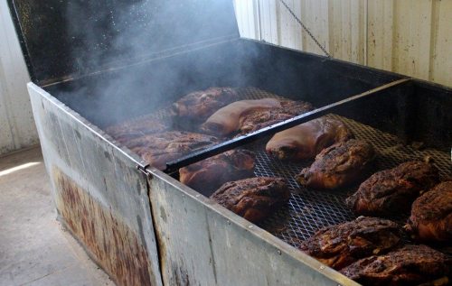 A large smoker filled with various cuts of meat, emitting smoke in a rustic setting.