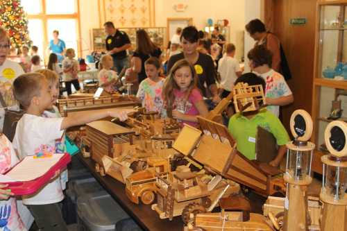 Children explore a variety of wooden toys and models at a workshop, with adults supervising in a festive setting.