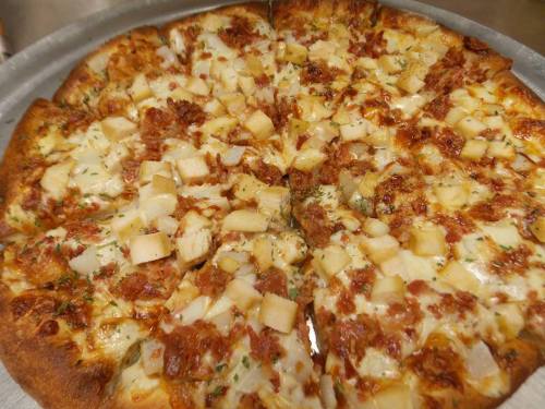 A freshly baked pizza topped with chunks of chicken, pineapple, and melted cheese, sliced into equal pieces.