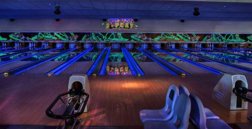 A vibrant bowling alley with glowing lanes and colorful decor, featuring empty seating and reflections on the polished floor.