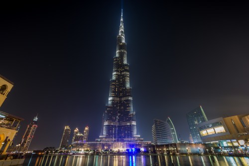 The Burj Khalifa illuminated at night, towering over the Dubai skyline with reflections in the water below.