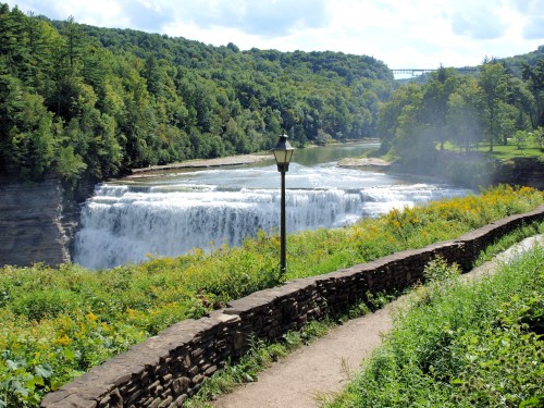 A scenic view of a waterfall surrounded by lush greenery and a stone pathway, with a lamp post nearby.