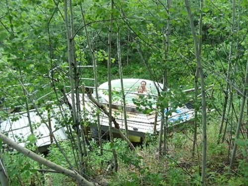 A person stands on a wooden platform surrounded by trees, with a green structure in the background.