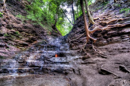 A rocky canyon with steep walls, lush greenery above, and a small waterfall trickling down the stone surface.