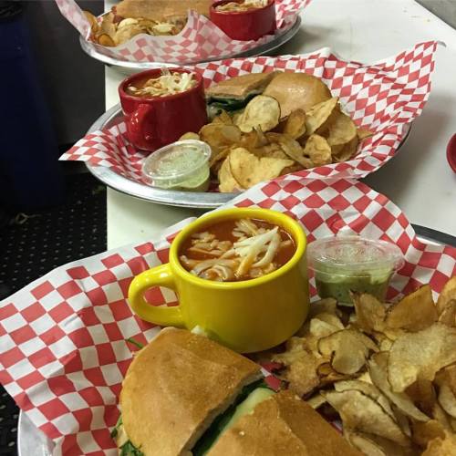 A colorful meal featuring sandwiches, chips, and a bowl of soup, all served on checkered trays.