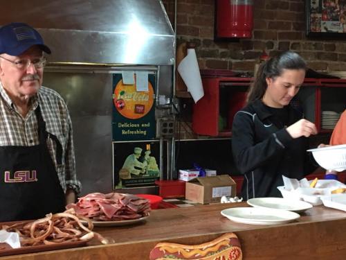 A man and a woman prepare food at a counter, with various meats displayed in front of them.