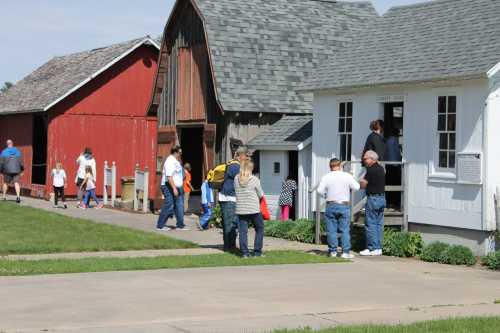 A group of people walking and interacting outside historic buildings on a sunny day. Green grass in the foreground.