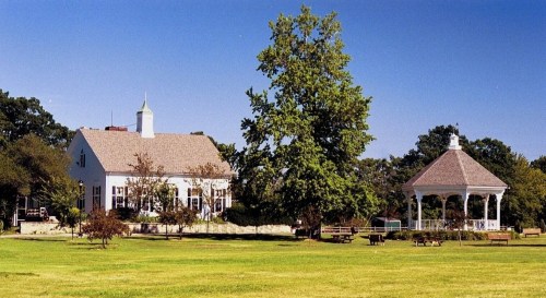 A white building and a gazebo surrounded by green grass and trees under a clear blue sky.