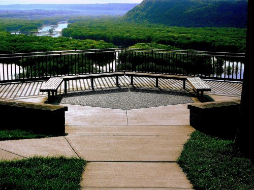 A scenic overlook with benches, surrounded by lush greenery and a river winding through the landscape.
