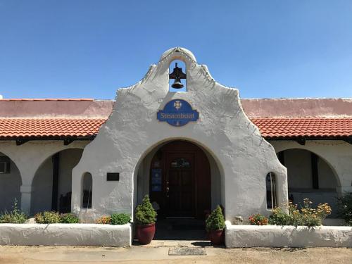A southwestern-style building with a bell tower, arched entrance, and colorful flower pots in front.