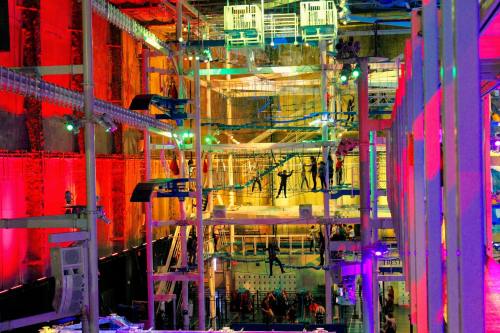 A vibrant indoor climbing facility with colorful lights, featuring climbers on various walls and structures.