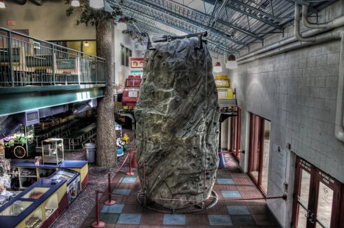 Indoor climbing wall in a recreational space, surrounded by seating areas and colorful decor.