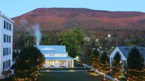 A scenic view of a mountain with autumn foliage, featuring a white building with smoke and trees adorned with lights.