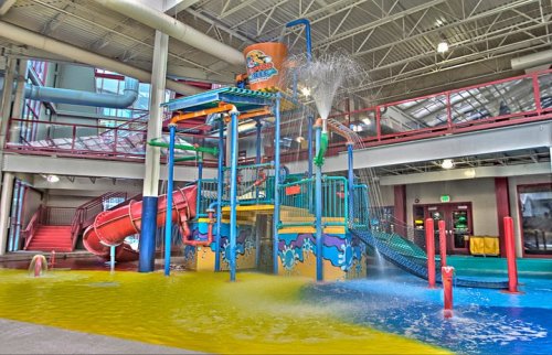 Colorful indoor water play structure with slides, water features, and a splash zone.