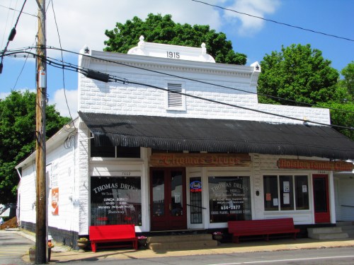 Historic building with "Thomas Drugs" signage, featuring a white exterior and red benches outside. Year "1915" displayed.