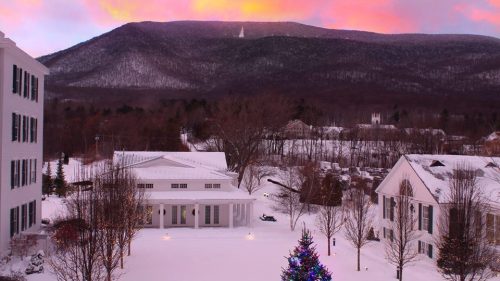 A snowy landscape with a Christmas tree, mountains in the background, and a colorful sunset sky.