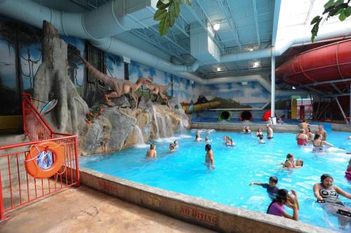 Indoor water park scene with a dinosaur-themed mural, featuring a pool and slides, filled with people enjoying the water.