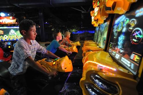 Children playing arcade games in a colorful gaming center, focused on the screens in front of them.