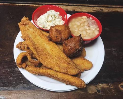 A plate of fried fish, hushpuppies, coleslaw, and baked beans served in red bowls.