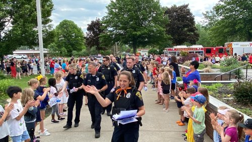 A group of police officers walks through a crowd of children clapping and cheering at a community event.