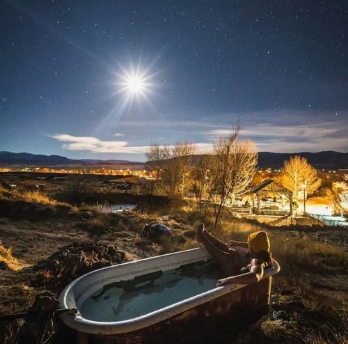 A person relaxes in a vintage bathtub under a starry night sky, illuminated by a bright moon.
