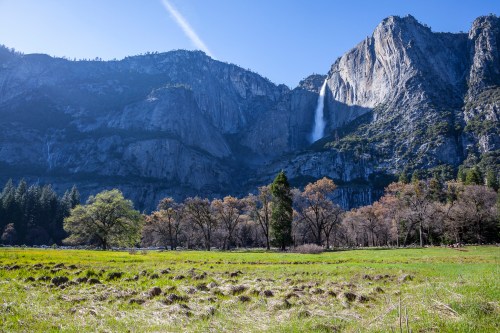 A scenic view of a mountain landscape with a waterfall, green meadow, and trees under a clear blue sky.