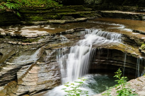 A serene waterfall cascades over rocky cliffs into a tranquil pool, surrounded by lush greenery.