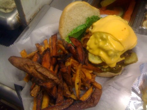 A cheeseburger with lettuce and pickles beside a serving of crispy fries on a white paper plate.