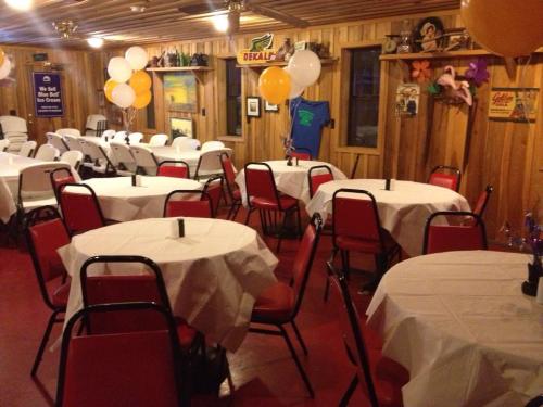 A cozy event space with round tables covered in white tablecloths, red chairs, and balloons in a rustic wooden setting.