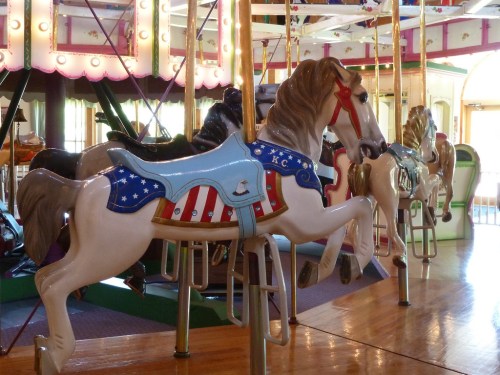 A colorful carousel featuring intricately painted horses with various designs, set in a bright amusement park.