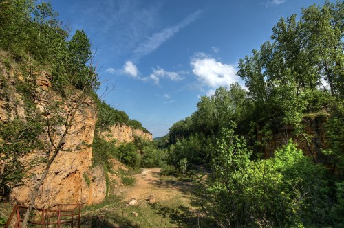 A scenic view of a lush green valley surrounded by rocky cliffs under a bright blue sky with scattered clouds.