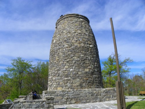 A tall, cylindrical stone tower surrounded by trees under a blue sky with wispy clouds.