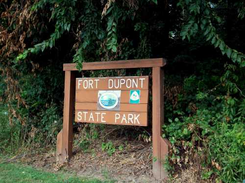 Sign for Fort Dupont State Park surrounded by greenery, featuring park logos and a wooden structure.