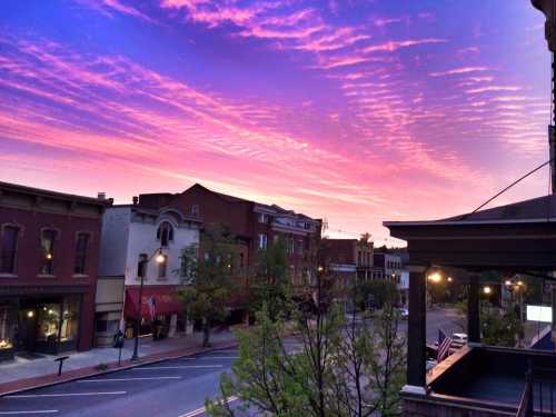 A vibrant sunset paints the sky in pink and purple hues over a charming street lined with historic buildings.