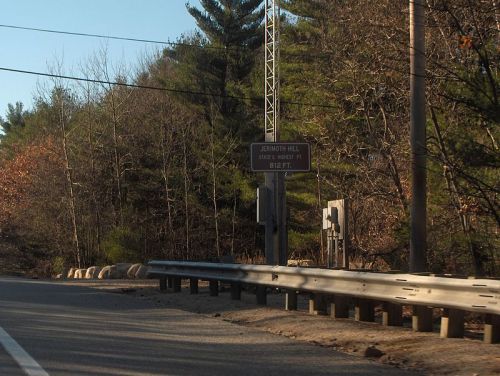 Roadside sign for Johnson Hill, with trees and a clear sky in the background.
