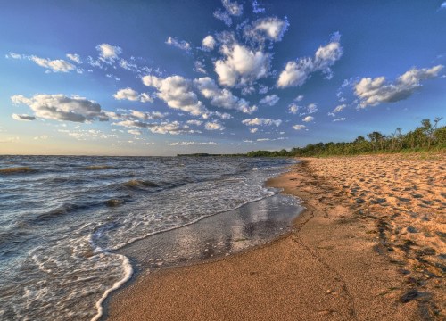 A serene beach scene with gentle waves, sandy shore, and a sky filled with fluffy clouds at sunset.