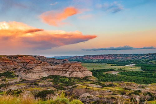 A scenic landscape featuring layered rock formations, lush greenery, and a colorful sunset sky.
