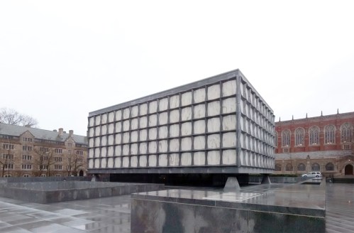 A modern, geometric building with a grid-like facade, surrounded by a reflective plaza and historic architecture in the background.