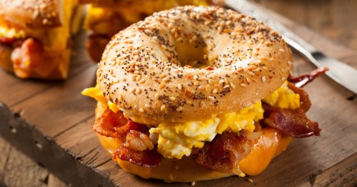 breakfast sandwich with egg, bacon, and cheese on an everything bagel on a wooden cutting board