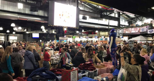 A crowded indoor market with people shopping and browsing various stalls and merchandise.