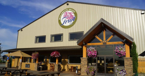 Exterior of a building with a sign reading "Marquette Valley Fruit Co," featuring flower baskets and outdoor seating.