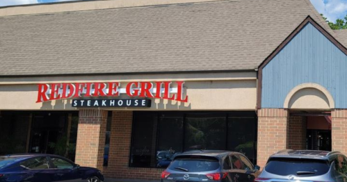 Exterior of Redfire Grill Steakhouse, featuring a sign and parked cars in front of a brick building.