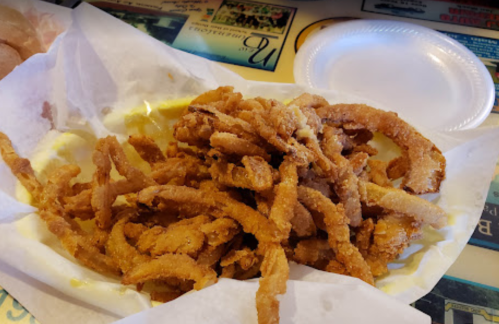 A serving of crispy, golden-brown onion strings in a paper tray, with a side of dipping sauce.